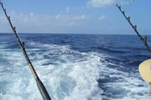 Two fishing rods over the wake of a boat on a family vacation in the open ocean under a blue sky.