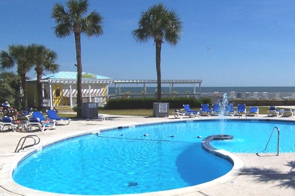 Outdoor swimming pool with blue lounge chairs, palm trees, and beach view—perfect for a Fripp Island family vacation.