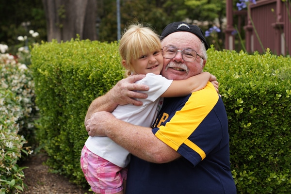 Smiling older man hugging a young girl outdoors in front of green bushes on a Lowcountry South Carolina vacation.