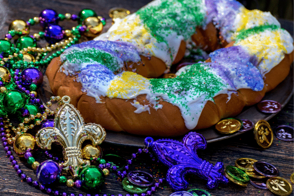 Colorful king cake with icing, sprinkles, Mardi Gras beads, and gold coins on a lowcountry wooden table.