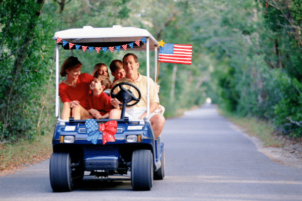 Family enjoying a south carolina vacation, riding a decorated golf cart with American flags down a tree-lined road.