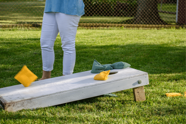 Person playing cornhole, tossing bean bags toward a white board on grass during a sunny South Carolina vacation.