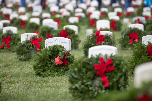 Rows of white gravestones with wreaths and red bows, set on a grassy cemetery in the Lowcountry.