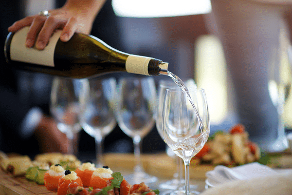 A hand pours white wine into a glass near appetizers on a wooden board, capturing the spirit of a Lowcountry beach vacation.