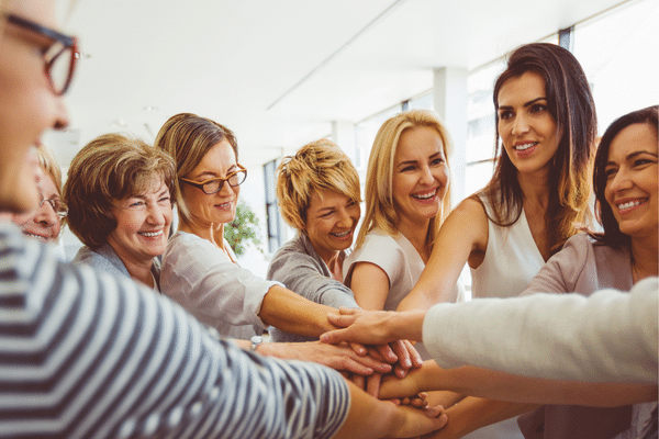 A group of women smiling and stacking their hands together during a Fripp Island beach vacation.