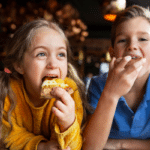 Two children, a girl and a boy, happily eating pizza slices during a family vacation on Fripp Island.