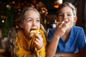 Two children, a girl and a boy, happily eating pizza slices during a family vacation on Fripp Island.