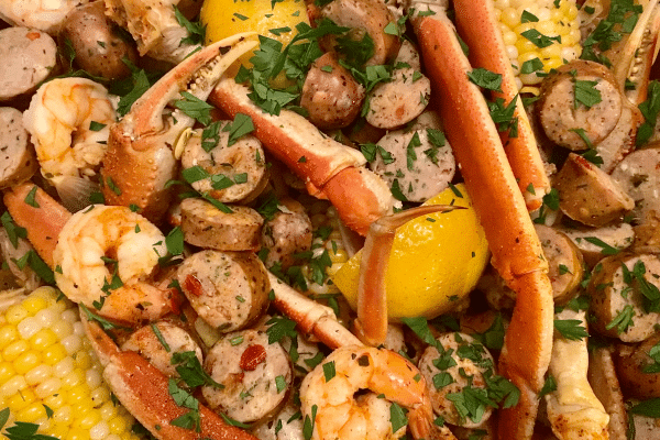 Close-up of a seafood boil with crab legs, shrimp, sausage, lemon, corn, and parsley.