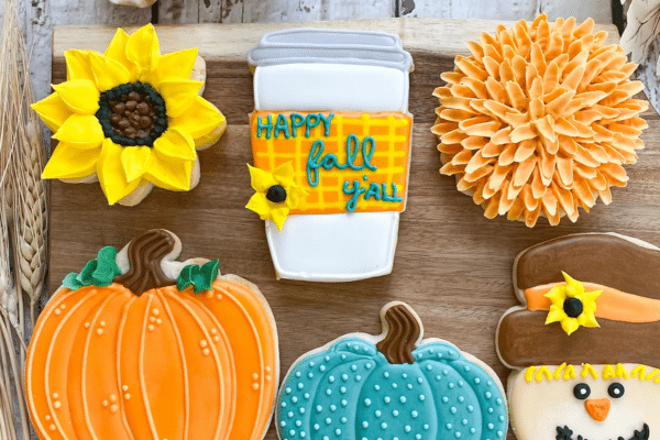 Decorated fall-themed cookies shaped like a pumpkin, flower, coffee cup, sunflower, and a scarecrow.