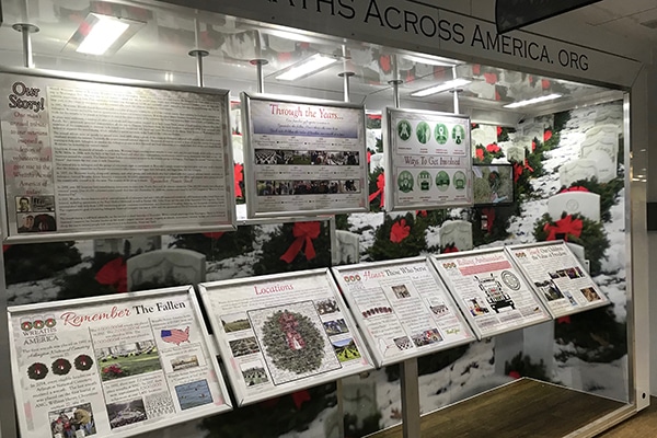 Exhibit display with information panels about Wreaths Across America, featuring wreaths and red bows as decoration.