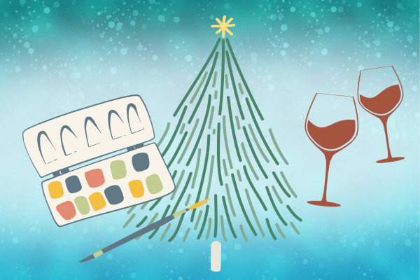 Watercolor paints, a brush, and two wine glasses next to a decorated Christmas tree on a blue background.