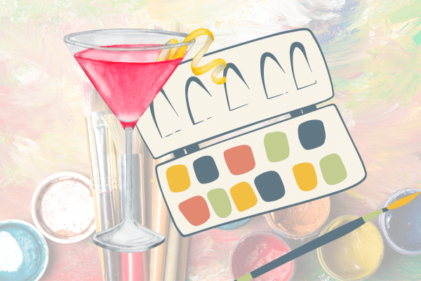 A cocktail, paintbrushes, watercolor palette, and paints on an artistic, colorful background.