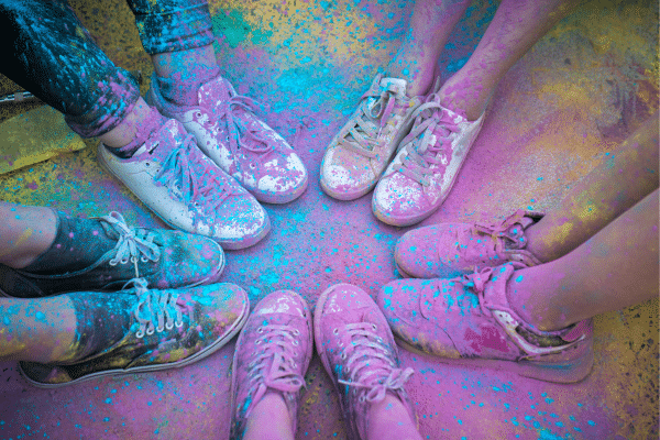 People wearing sneakers stand in a circle, their shoes and legs covered in bright colored powder.