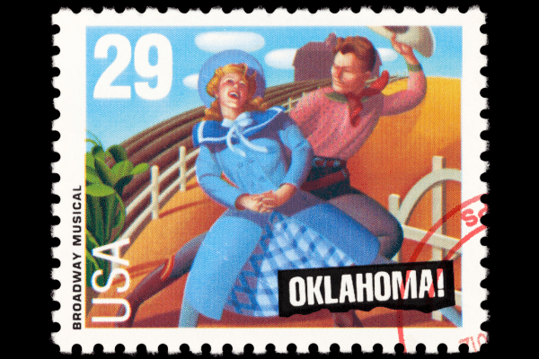 Postage stamp showing a scene from the musical Oklahoma with a man and woman in frontier attire, evoking a beach vacation.