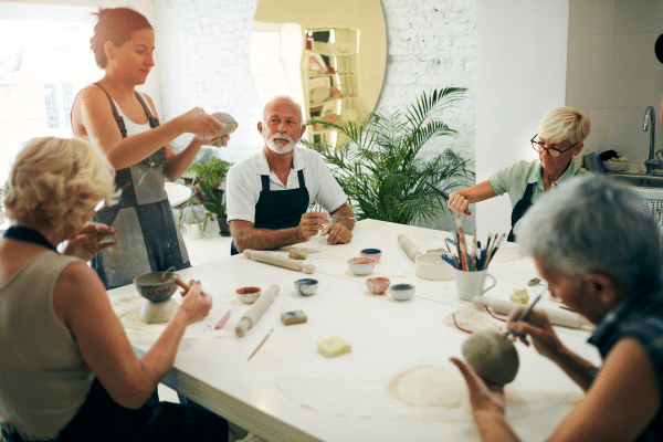 Five older adults make pottery together at a table, with an instructor assisting, during a lowcountry family vacation.