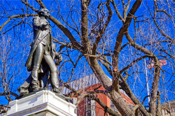 Bronze statue of a man in colonial attire stands before leafless trees on a lowcountry south carolina vacation.