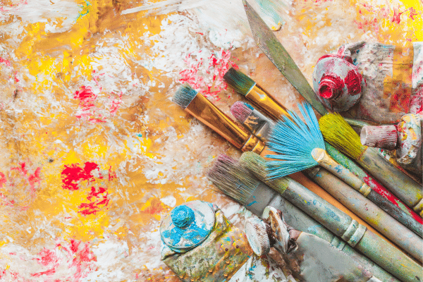 Assorted paintbrushes and paint tubes on a colorful, paint-splattered surface evoke a vibrant Lowcountry vibe.