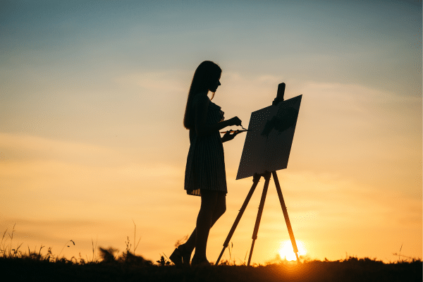 Silhouette of a woman painting on an easel outdoors during a Fripp Island sunset.