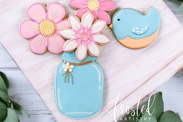 Iced cookies shaped like flowers in a blue jar with a blue bird, evoking Lowcountry charm on a light wooden surface.