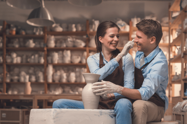 A smiling couple in aprons makes pottery together, evoking a cozy South Carolina vacation vibe.