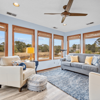 Bright sunroom with large windows, cozy seating, a blue rug, a pouf, and a telescope facing outside.