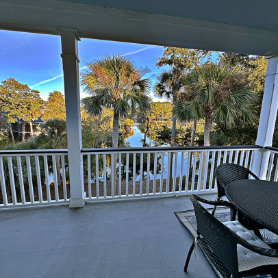 View from a porch with table and chairs, overlooking palm trees and calm water at a Fripp Island vacation rental.