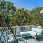 Outdoor deck with cushioned seating, a swing, and trees in the background under a clear blue sky.