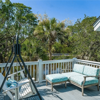 Outdoor deck with cushioned seating, a swing, and trees in the background under a clear blue sky.