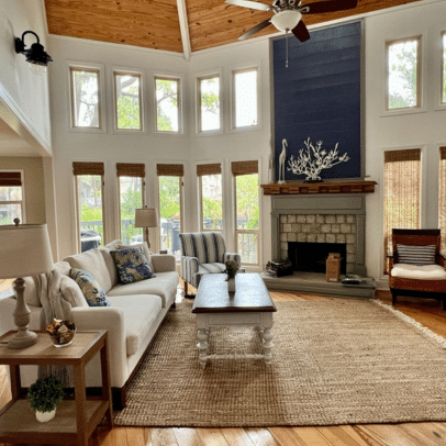 Bright living room with tall windows, a white sofa, fireplace, armchairs, and a jute rug on hardwood floors.