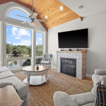 Living room with large windows, a fireplace, a mounted TV, and a wooden ceiling with exposed beams.