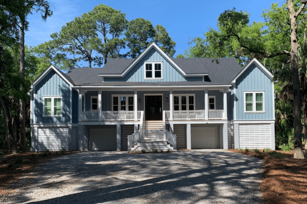 Blue two-story house with white trim, triple garage doors, and a front porch surrounded by trees.