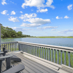 Deck with chairs overlooks a calm river, green marsh grass, blue sky, and scattered clouds.