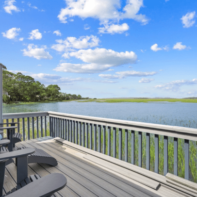 Deck with chairs overlooks a calm river, green marsh grass, blue sky, and scattered clouds.
