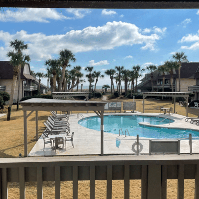 View of a sunny outdoor pool with lounge chairs, palm trees, and buildings in the background.