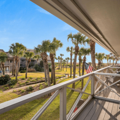 View from a balcony with palm trees, grassy area, and an American flag under a clear blue sky.