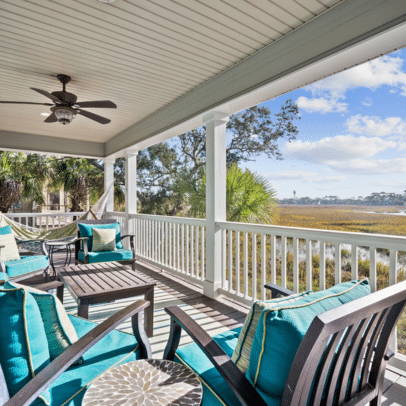 Covered porch with teal cushioned chairs, ceiling fan, and view of marshland and blue sky.