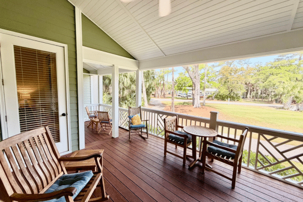 Spacious porch with wooden chairs, small tables, and a green yard view on a sunny day.