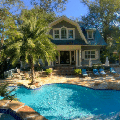 A house with a pool, palm trees, lounge chairs, and umbrellas on a sunny day.