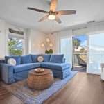 Living room with blue sectional sofa, round wicker table, rug, ceiling fan, and balcony with outdoor seating.
