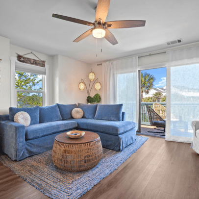 Living room with blue sectional sofa, round wicker table, rug, ceiling fan, and balcony with outdoor seating.