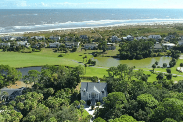 Aerial view of a coastal neighborhood with greenery, houses, a golf course, and the ocean in the background.