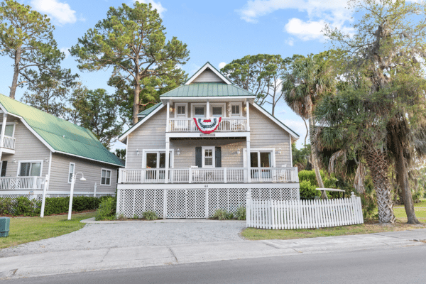 Gray two-story house with a porch, white fence, and patriotic bunting hanging above the entrance. Golf Vacation rental on Fripp Island.