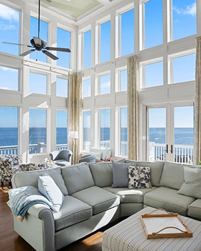 Spacious living room with large windows, ocean view, light sofa, and ceiling fan.