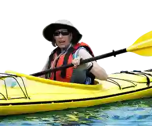 Person in sun hat and life jacket paddling a yellow kayak on the water, holding a yellow paddle.