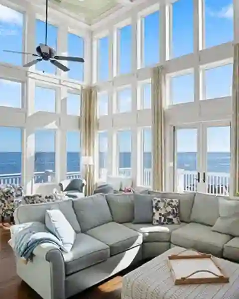 Bright coastal living room with large windows, grey sectional sofa, ocean view, and ceiling fan.