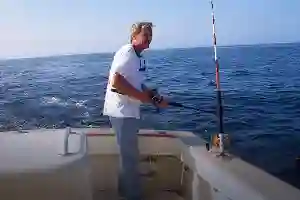 Man fishing from a boat in the ocean under a clear sky.