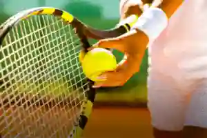 Close-up of a tennis player holding a racket and tennis ball, preparing to serve on a court.